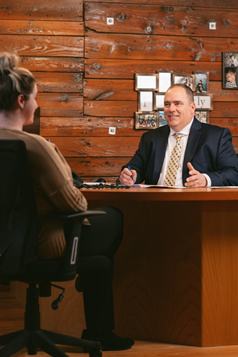 Tim Hayes chats with a client at his desk. Images from behind him show a family collage and he is smiling as he speaks.