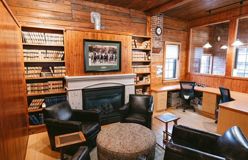 Tim Hayes Law interior office space with four chairs around a circular table next to a fireplace. There are shelves that sandwich the fireplace on either side filled with lawbooks and the walls themselves are all wooden panels like a log-cabin, giving off a warmer, welcoming atmosphere.